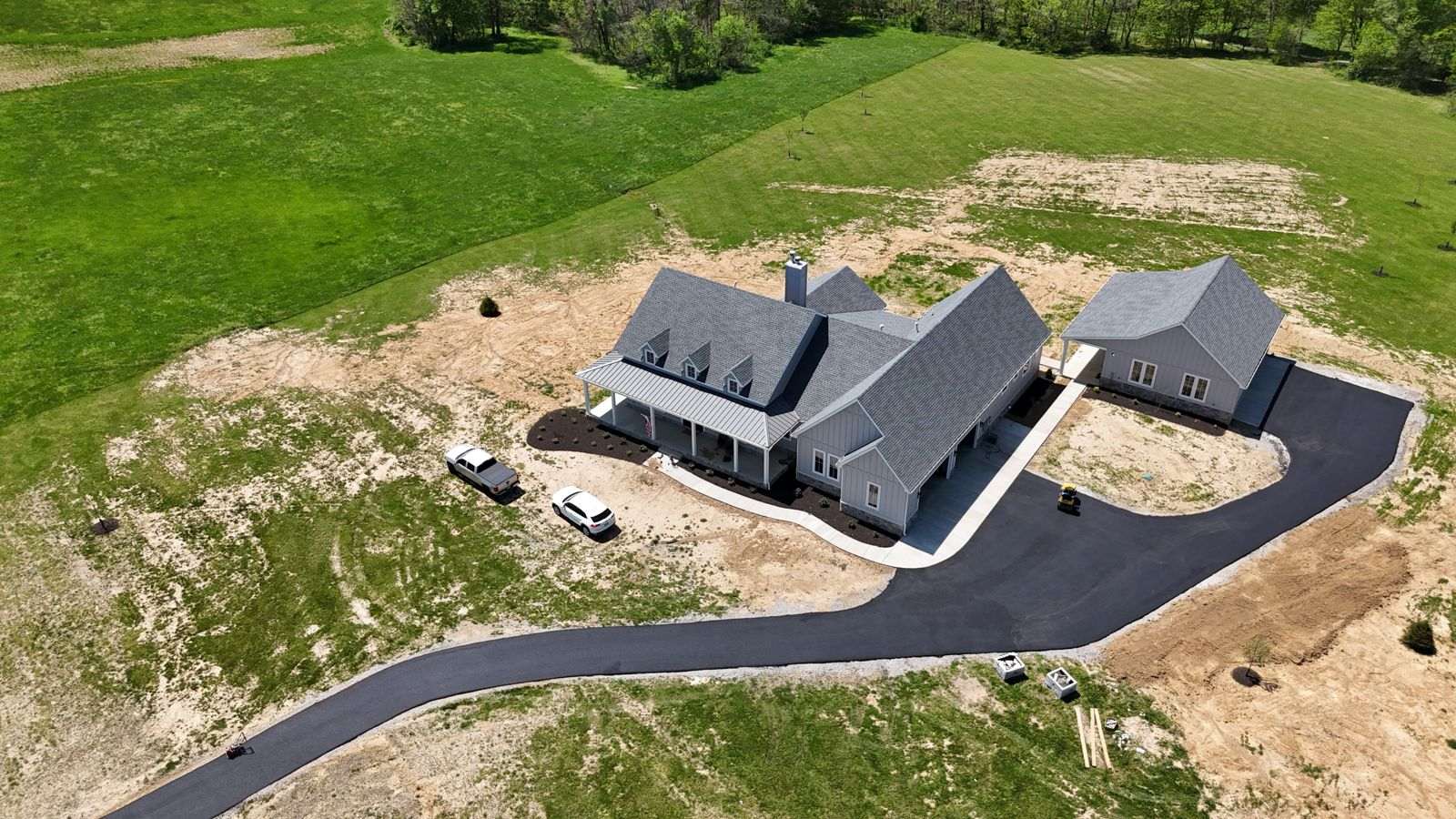Drone view of a new home with a fresh asphalt driveway curving through bare ground