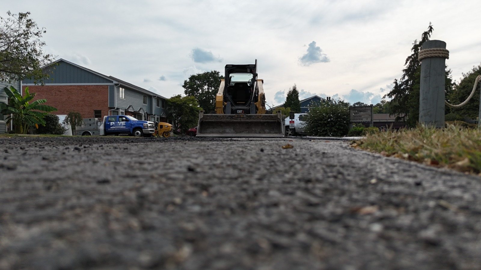 Ground-level view of fresh asphalt with a skid steer and a Pave It Forward truck